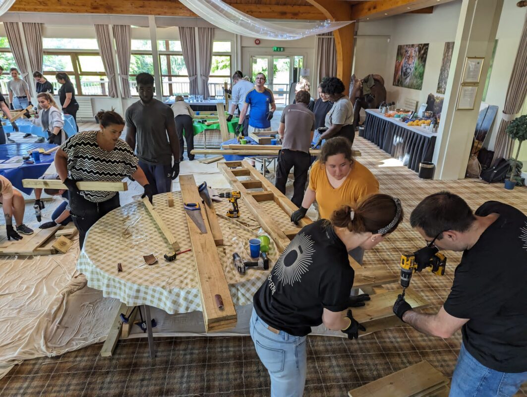 “Corporate group engaging in a CSR activity overlooking the wildlife habitats at Woburn Safari Park.” “Employees collaborating during a team building session at Woburn Safari Park’s Safari Lodge event space.”